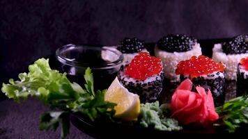 Sushi with red and black caviar Close-up of uramaki sushi rolls with red caviar, salmon, cucumber and avocado isolated on a black background. Delicious traditional Japanese food with sushi rolls. video