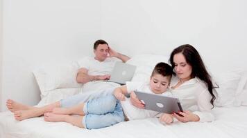 freelance work allows family to be together father works on laptop in bed at home mom and son play on tablet have time with family parents have fun relaxing man earn money isolated on white background video