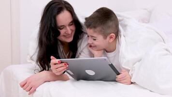 mom and son under white blanket watching funny on tablet playing game family comfort caring father working mom and son at home life insurance safety having fun mortgage love happy family video