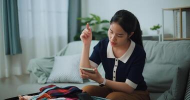 Selective focus of Asian teenager woman sitting on sofa making checklist of things to pack for travel, Preparation travel suitcase at home. photo