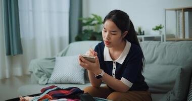 Selective focus of Asian teenager woman sitting on sofa making checklist of things to pack for travel, Preparation travel suitcase at home. photo