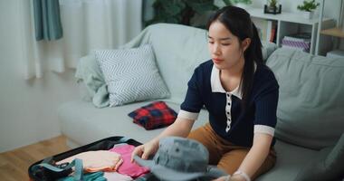 Portrait of Asian teenager woman sitting on sofa packing travel luggage with personal items for traveling trip, Preparation travel suitcase at home. photo