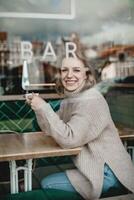 sonriente mujer disfrutando café en cafetería. un alegre mujer se sienta a un café mesa, participación un taza de café con un visible bar firmar en el antecedentes. calor y relajación exudar desde el acogedor atmósfera. foto