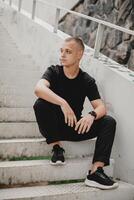 A man in a black shirt and black pants sits on a set of stairs photo