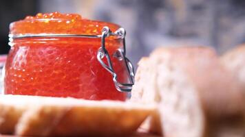 met een mes naar verspreiding boter Aan brood in de achtergrond een glas pot met kaviaar dun gesneden baguette met Zalm kaviaar en boter, heerlijk belegd broodje met brood, boter en natuurlijk rood kaviaar video