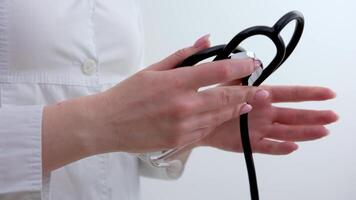 Hands of a woman doctor folding a phonendoscope and leaning against her shoulder Stethoscope on white background, top view. Space for text video