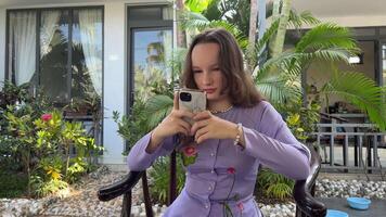 européen fille avec une téléphone dans une vietnamien asiatique costume contre le toile de fond de une Hôtel avec paume des arbres utilisation le téléphone sur social réseaux communiquer avec copains attendre video