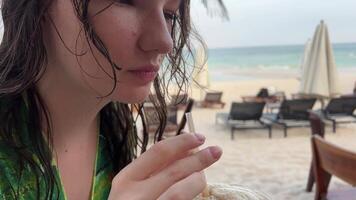 en flicka med bra glädje drycker en kaffe dryck på de strand visar henne fingrar bara perfekt Okej hon visar strålar de glädje av liv nöje från avkopplande i en grön pareo med våt hår efter simning video