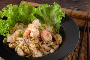 Closed up stir-fried rice noodle with chicken, shrimp and egg and vegetable on wooden table, Chinese easy cooking photo