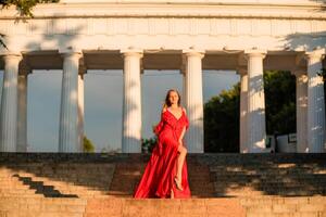 A woman in a long red dress against the backdrop of sunrise, bright golden light of the sun's rays. The concept of femininity, harmony. photo