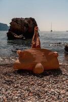 un hermosa de edad mediana mujer mentiras en el playa con su pies a el cielo, cubierta su cuerpo con un de ala ancha Paja sombrero. ella es broncearse en el océano. vacaciones, viajar, vacaciones concepto. foto