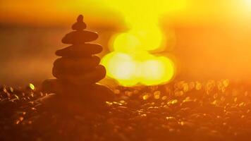 Balanced rock pyramid on pebbles beach. Golden sea bokeh on background. Selective focus, zen stones on sea beach, meditation, spa, harmony, calm, balance concept. photo