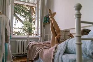 Woman reading a book in bed, lying on her stomach smiling happy and relaxed on a leisure day at home photo