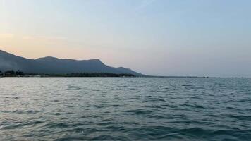 A view from a moving boat across the water of fish farms built on a lake with a small house with a roof, standing on the water. Overlooking the volcano in the background. The camera is moving around. video