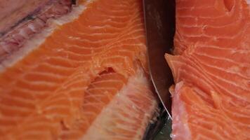 Hands cooks close-up. The chef cuts with a knife a red fish, smoked salmon on a wooden cutting board. Black wooden table on background. video