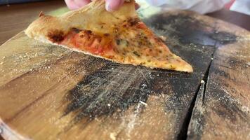 Hand taking the last piece of thin crispy pizza on wooden plate with blackboard video