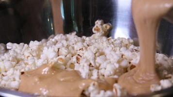 cooking popcorn at home in a special machine caramel filling caramelized popcorn recipe close-up delicious treat for movie stir and pour caramel icing popcorn grains iron utensil appetizing snack video