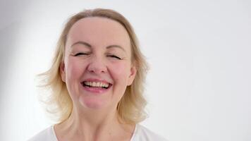 gezicht van een middelbare leeftijd vrouw met blond haar- Aan een wit achtergrond detailopname ze verlaagd haar ogen vriendelijke groet glimlacht reliëf twijfel vreugde tederheid schoonheid rust vrede video