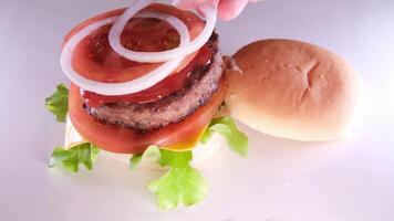 falten ein Burger erstellen ein Burger Startseite mit ein Brötchen stellen Zwiebel Schnitzel Tomate gießen Senf Ketchup stellen Käse und Grüner Salat Verbreitung Mayonnaise auf das Brötchen das ganze Prozess im anders s video