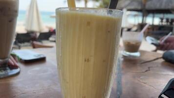 utsökt is latte kaffe mango smoothie på en havet i sommar. kall dryck på strand Kafé utomhus. resa och njut av bali ö. video