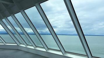 Bakom de glas du kan ser de hav eller de hav en stor fönster av en fartyg eller en färja eller en stor hotell byggnad genom som du kan ser de himmel och de blå hav en damm är en mycket skön se video