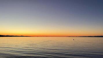 sunset on the Ocean Calmness calm sea on Vancouver Island resting in trailers on the shore bright colors of dark blue orange stripe on the horizon from the sun rich space for text travel advertising video