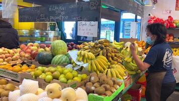 granville isola un asiatico donna nel un' maschera con un grembiule e un' blu maglietta sembra a il elenco quello lei esigenze per acquistare a il drogheria bazar lei prende banane a partire dal il mercato e mette sua Borsa giù video