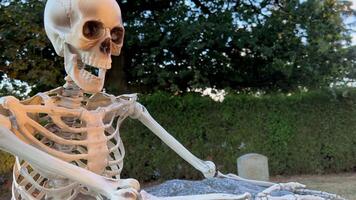 The skeleton stands near the tombstone and holds on to it looks down it is in the cemetery Halloween holiday in autumn it is possible to use it as a background for some text the camera slowly floats video