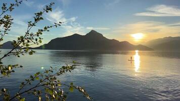 A man on a canoe sailing far Porteau Cove Provincial Park Canada Vancouver As the sun is seen as the sun sets behind the mountains on left side of the leaves of the tree beautiful nature Pacific ocean video