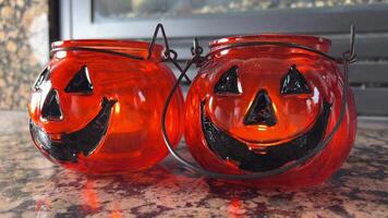 Two bright orange candlesticks in the form of pumpkins Jack-o-lantern Glass lantern with real candles Black eyes and black smile Transparent orange glass Standing on mottled brown marble video