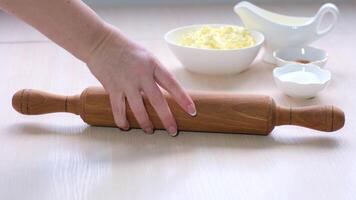 woman takes rolling pin from table and puts dough yeast approached fermentation she swings it on light table sprinkled with flour against the background ingredients sprinkles the dough with flour video