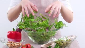 young girl mixes lettuce with hands she pours into glass plate vegetarian food wooden spoons apron tablecloth white background young woman teenager prepares dinner for family dinner breakfast lunch video