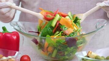 menging heerlijk smakelijk salade met wortels gesneden paprika's verschillend Groenen olijven en noten detailopname onherkenbaar vrouw roert met groot houten lepels in handschoenen video