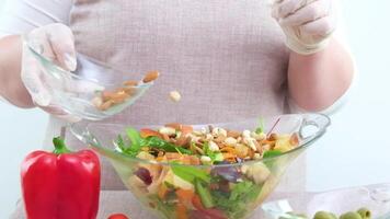 woman prepares vegetarian salad in kitchen slowly adding nuts to cashew salad almonds hazelnuts woman in gloves cook aprons vegetables ingredients Glassware Healthy food vegetarian tasty and vitamin video