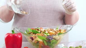 The chef season and sprinkles with pine nuts a salad of vegetables, herbs, nuts in a transparent plate. Woman's hand sprinkles pine nuts salad. Close-up in slow motion, colorful. video