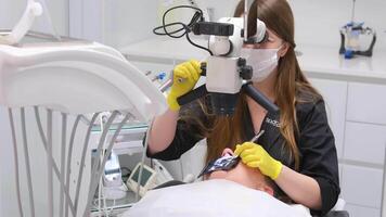 el utilizar de un microscopio en raíz canal relleno europeo medio satisfecho dentista mujer en cara máscara trabajando en dental clínica video