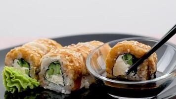 Dunk one sushi roll in soy sauce on black background. Closeup video