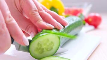 fêmea mãos fechar-se corte uma pepino em uma branco porcelana borda dentro volta círculos com argolas cozinhando inscrição em a olhos cozinhando salada video