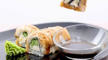 Big sushi rolls with salmon in nori, crab sticks, cucumber, Philadelphia cheese dipped in a bowl of soy sauce with the help of bamboo sticks close up view video