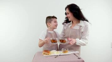 ung mor har frukost på Hem i de kök tabell medan spelar med bebis. avkopplande ljuv familj ögonblick mellan mamma och son i de morgon- har kaffe eller te video