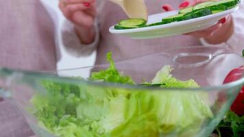 mother and child preparing vegetable salad close-up boy's hands help mother to add cucumbers glass plate Professional female cook adding fresh cucumber slices in glass bowl with salad video