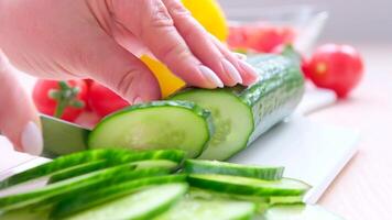 Woman cuts a green cucumber on a cutting board. On the table are vegetables video