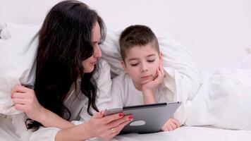 mom and son under blanket playing on tablet laugh smile games internet online learning educational activities spend time together in the family at home recover skip school at kindergarten day off video