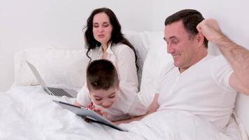 husband wife and son spend time together in bed holiday look at tablet communicate conversation love at home happiness joy success in gadgets white background place for advertising text happy family video