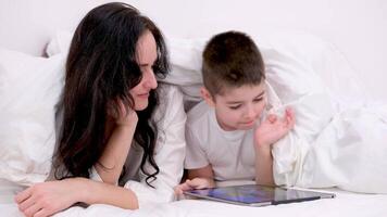 mom and son under blanket playing on tablet laugh smile games internet online learning educational activities spend time together in the family at home recover skip school at kindergarten day off video