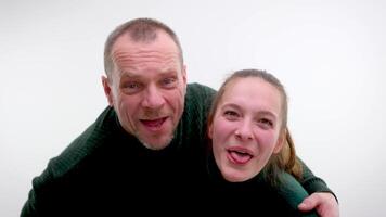 man and girl leaned over and stuck out tongues in background light for photography father and daughter teacher and student husband wife green sweaters fun making faces grimacing showing tongue video