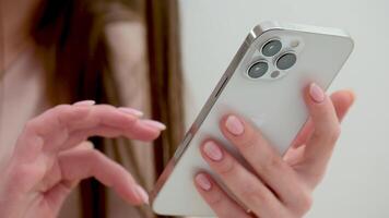 close-up of a girl's hands scrolling through a page on a smartphone from top to bottom flipping search adjust the volume touchpad press a finger on the phone white gadget study business manicure video