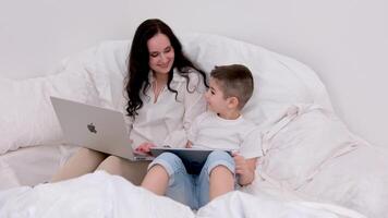 conectados Treinamento usando maçã ipad e macbook tecnologia dentro a mãos do uma mulher e filho sentado em uma suave cama dentro uma caseiro acolhedor atmosfera jogar trabalhos conectados vida em a Internet video