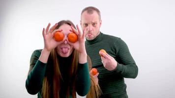 young girl put Tangerines to eyes and pulled out tongue stuck out and she twists and makes faces in the background a man on a white background a green sweater long hair joke fooling around grimacing video