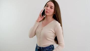 Smiling millennial woman talking on the phone at home, happy young girl holding a mobile phone while answering a call, attractive teenager talking nicely on a cell phone with a friend video